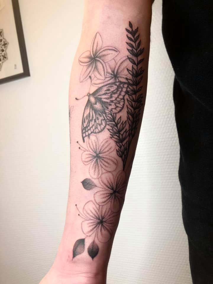 Un tatouage d'un papillon et plusieurs fleurs en travail de points sur tout l'avant-bras